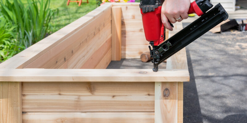 Wooden raised bed being constructed with person holding a power tool